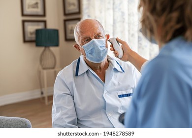 Senior man wearing face mask for safety against covid-19 and getting ear temperature checked by nurse at home. Nurse checking ear temperature of old patient using electronic tympanic thermometer.  - Powered by Shutterstock