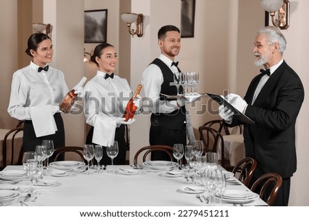 Senior man wearing formal suit teaching trainees in restaurant. Professional butler courses