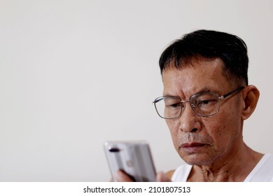 A senior man wearing glasses looks at a smartphone in his hand to read a message. at home alone