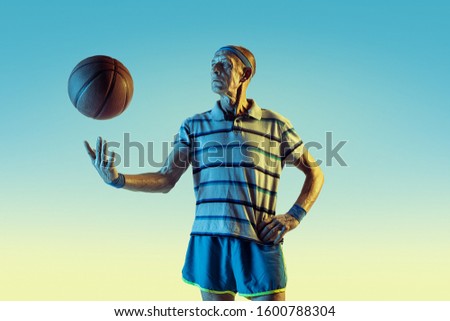Senior man wearing sportwear playing basketball on gradient background, neon light. Caucasian male model in great shape stays active. Concept of sport, activity, movement, wellbeing, confidence.