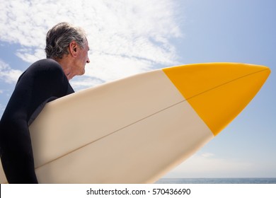 Senior man in wetsuit holding a surfboard and looking at a distance on the beach - Powered by Shutterstock