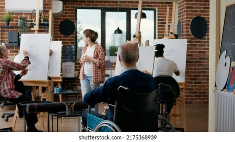 Senior Man In Wheelchair Attending Art Class Lesson As New Years Resolutions, Drawing Sketch On Canvas To Develop Artistic Skills. Student With Disability Using Tools To Draw Artwork.