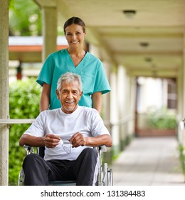 Senior Man In Wheelchair With Nurse On A Stroll Through The Hospital Garden