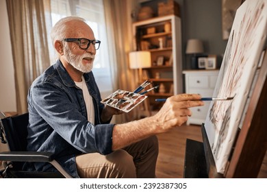 Senior man in a wheelchair painting on a canvas at home - Powered by Shutterstock