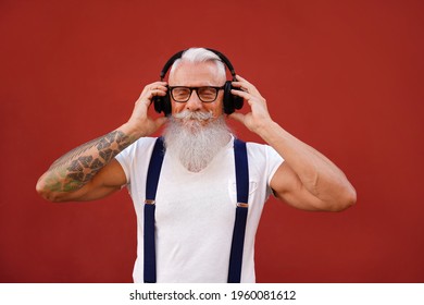 Senior man with white beard and mustache listening favorite music with headphones. People happy lifestyle and technology concept. Red background. Fashionable mature men.
        - Powered by Shutterstock