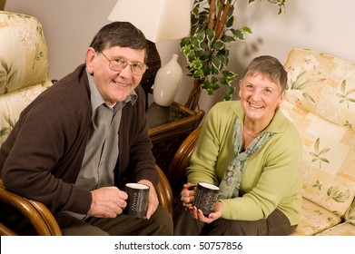 Senior Man And Woman Couple Relaxing On Sofa In Lounge, With Drinks Of Tea Or Coffee