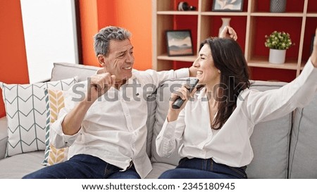 Senior man and woman couple singing song using tv remote control as a microphone at home