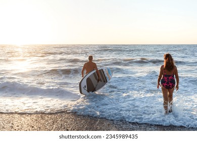 senior man and woman entering the beach with a surfboard at sunrise separately - Powered by Shutterstock