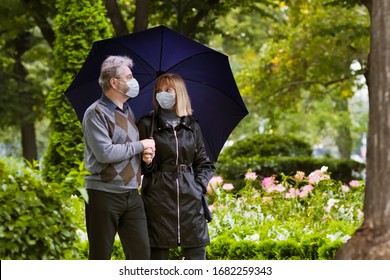 Senior Man And Woman In Face Mask. Virus Outbreak. Retired Couple Walking In A Park Under Quarantine During Coronavirus Outbreak. Surgical Masks To Prevent Sickness. People In Hospital Yard.