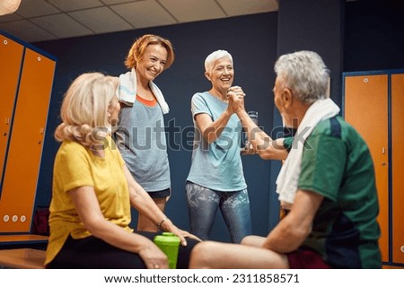 Senior man and woman high fiving in gym locker room, feeling energized for workout, mature woman and young woman cheering for them. Health concept.