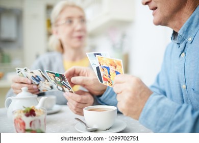 Senior Man And Woman Looking Through Photos Of Their Grandchildren While Having Tea