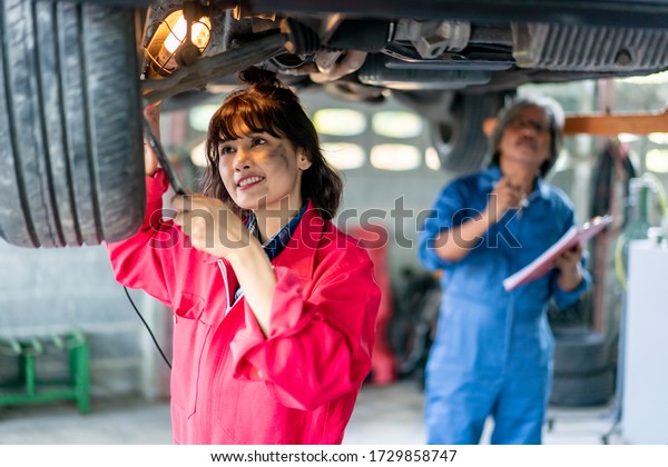 Senior Man and Woman Mechanic Examining Under the\
Car at the Repair Garage. Asian old man and young female checking\
and maintenance the\
car.\
