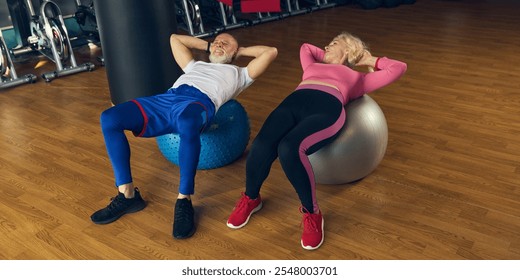 Senior man and woman in sportswear training in gym, lying on stability balls, performing core exercises together. Concept of elderly people, sport, active lifestyle, health - Powered by Shutterstock