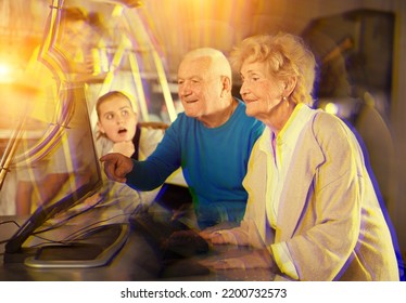 Senior man and woman using computer to solve conundrum in escape room. Their grandson standing on stepladder, granddaughter looking at grandparents.