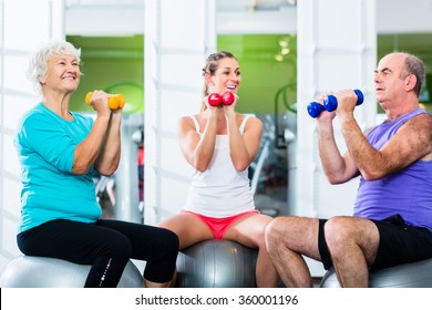 Senior Man And Women With Fitness Trainer In Gym Lifting Barbells As Sport Exercise