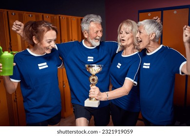 Senior man and women in sports uniform celebrating success with young woman trainer in gym locker room. Vicotry, senior team, sports concept. - Powered by Shutterstock