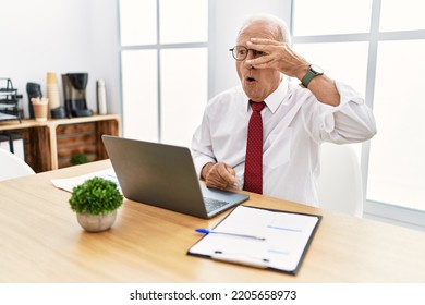 Senior Man Working At The Office Using Computer Laptop Peeking In Shock Covering Face And Eyes With Hand, Looking Through Fingers With Embarrassed Expression. 