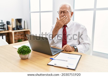 Senior man working at the office using computer laptop bored yawning tired covering mouth with hand. restless and sleepiness. 