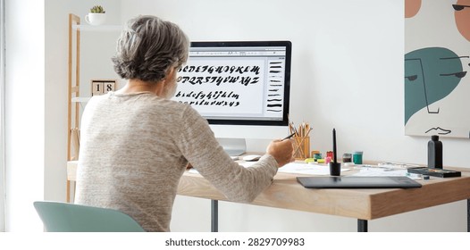 Senior man working on a computer with a graphics tablet, designing calligraphy fonts and digital artwork at home
