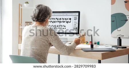 Senior man working on a computer with a graphics tablet, designing calligraphy fonts and digital artwork at home