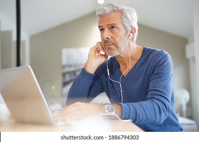 Senior Man Working On Laptop And Using Earphones For Virtual Meeting