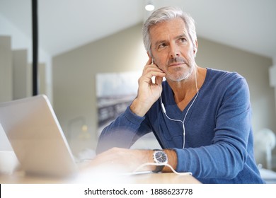 Senior Man Working On Laptop And Using Earphones For Virtual Meeting