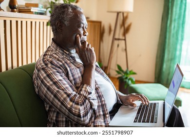 Senior man working on laptop at home in cozy living room - Powered by Shutterstock