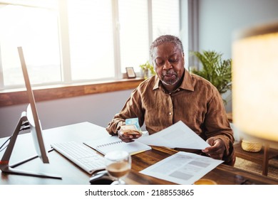 Senior Man Working At PC Computer At Home. African American Man Calculating Finances. Shot Of A Mature Man Going Through Some Paperwork At Home