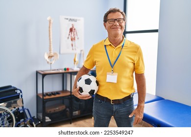 Senior man working at sport physiotherapy clinic looking positive and happy standing and smiling with a confident smile showing teeth  - Shutterstock ID 2253549247