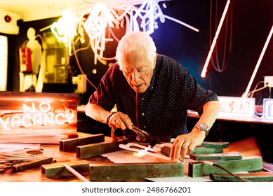 A senior man works on a neon sign in his workshop. He uses a blowtorch to bend the glass tubing for the sign, which reads No Vacancy. - Powered by Shutterstock