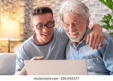 Senior man and young boy smiling and looking together at laptop at home. Happy nephew teaching and showing new computer technology to his old grandfather. Old man learn to use computer. - Powered by Shutterstock