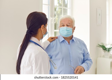 Senior Man And Young Female Doctor In Medical Face Masks Talking In Hospital Office. Physician In Modern Clinic Patting Aged Patient On The Shoulder, Supporting, Calming Down, Cheering Him Up