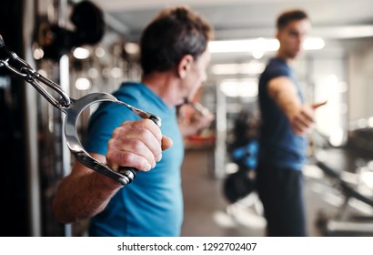 A Senior Man With A Young Trainer Doing Strength Workout Exercise In Gym.