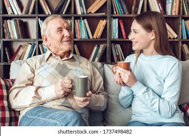 Senior man and young woman at home library sitting on sofa drinking hot tea smiling joyful talking about life - Powered by Shutterstock