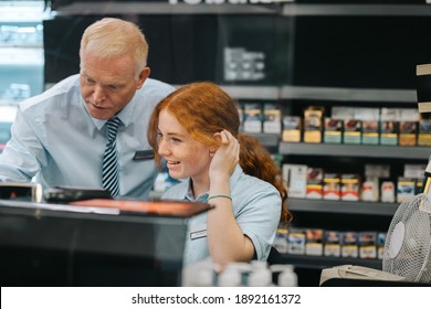 Senior Manager Giving Training To A New Female Employee At Checkout Counter. New Cashier Getting Some Help From Store Manager.