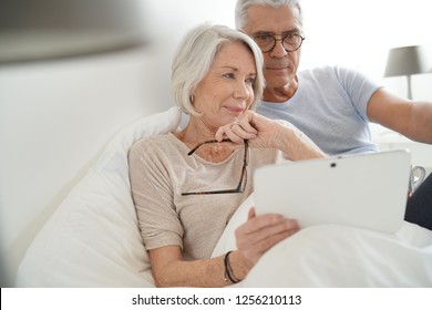 Senior married couple relaxing in bed looking at tablet                                - Powered by Shutterstock