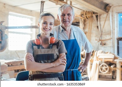 Senior master carpenter with his granddaughter in the wood workshop looking at camera