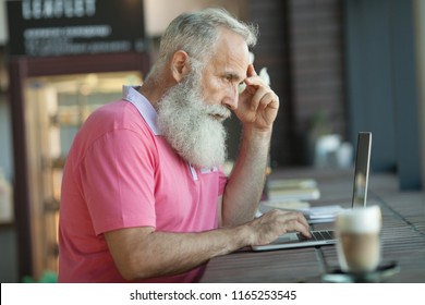 Senior Mature Business Man Having A Coffee In A Coffee Shop And Working On His Laptop