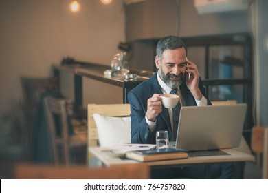 Senior Mature Business Man Having A Coffee In A Coffee Shop And Working On His Laptop