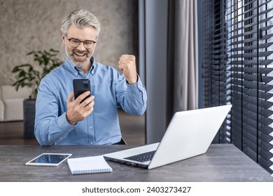 Senior mature businessman boss received online notification victory win, gray haired man holding phone, celebrating victory and successful achievement results workplace inside office, working laptop. - Powered by Shutterstock