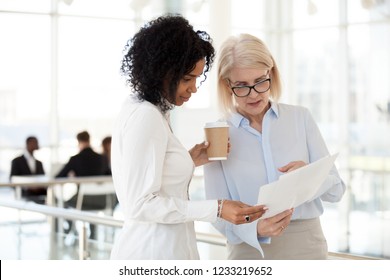 Senior Mature Caucasian Female Executive Ceo Discuss Report With Young Mixed Race Black Colleague, Serious Old Aged Mentor Reads Paper Explains Business Plan To African Employee Intern Talk In Office