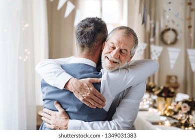 A senior and mature man standing indoors in a room set for a party, hugging. - Powered by Shutterstock