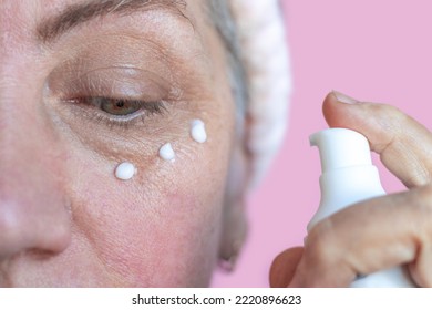 Senior Mature Old Elderly Lady With Rosacea Close Up Face Skin Care Applying Cream On Under Eye Bags Cheeks 3 Drops.granny  With Wrinkles Do Anti Age Procedures.woman Isolated On Pink Wearing Headband