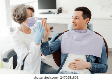 Senior mature woman dentist and smiling patient giving high five while sitting in modern dentistry. Attractive female orthodontist dental hygiene. Health care concept - Powered by Shutterstock