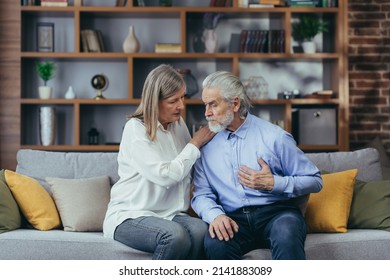 Senior Mature Woman Helping Her Husband With Chest Pain. Old Man Feeling Bad Pain Disease. Wife Supporting Husband - Elderly Couple Suffering From Symptoms Heart Attack Ache. Sitting At Home Indoors