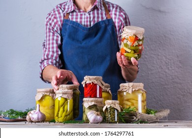 Senior mature woman holding in hands jar with homemade preserved and fermented food. Variety of pickled and marinated vegetables. Housekeeping, home economics, harvest preservation