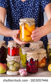 Senior mature woman holding in hands jar with homemade preserved and fermented food. Variety of pickled and marinated vegetables, fruit compote. Housekeeping, home economics, harvest preservation  