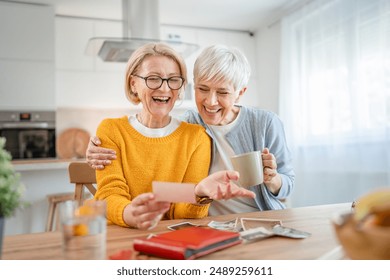 Senior mature women friends or sisters looking family photos album two caucasian females sit at home happy smile while revoke memories real people copy space - Powered by Shutterstock