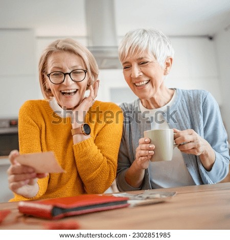 Senior mature women friends or sisters looking family photos album two caucasian females sit at home happy smile while revoke memories real people copy space