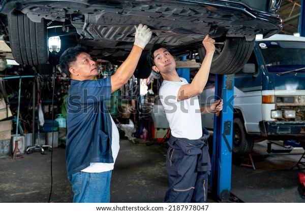 Senior mechanic and young man help to\
fix the problem of car in area under the car in\
garage.